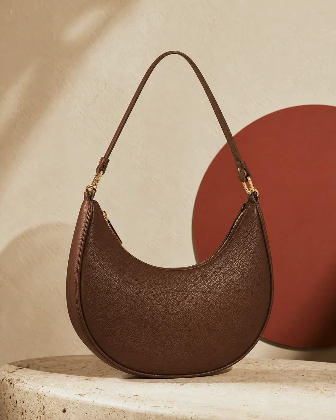 Cocoa crescent shoulder bag against a warm ivory studio wall