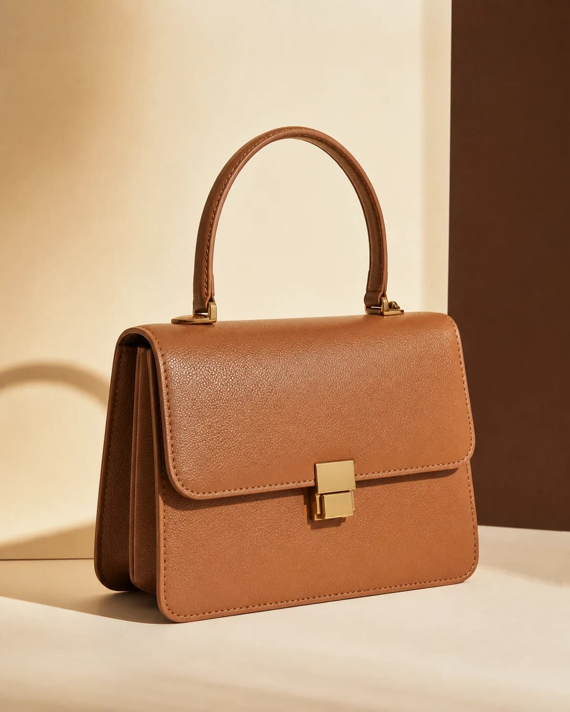 Warm tan structured top-handle handbag in an ivory studio setting